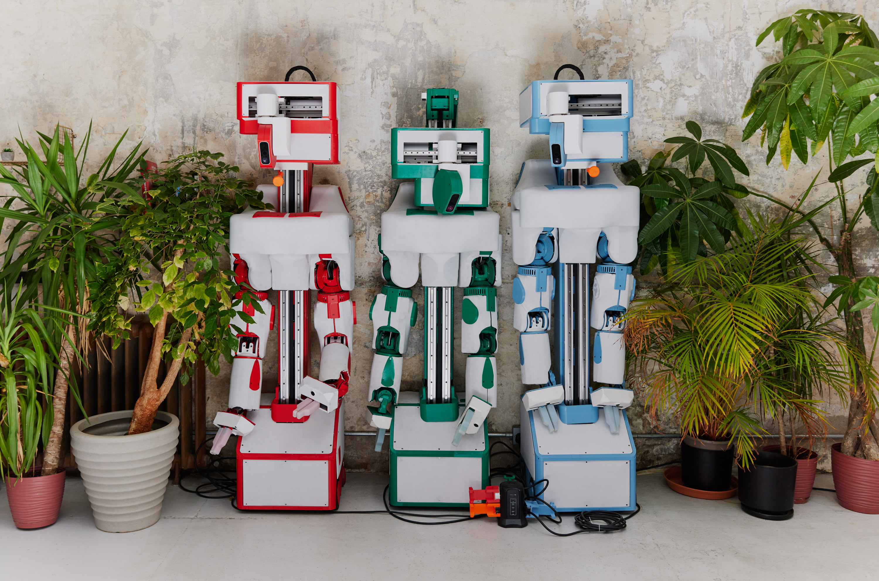 three robots against a wall between plants