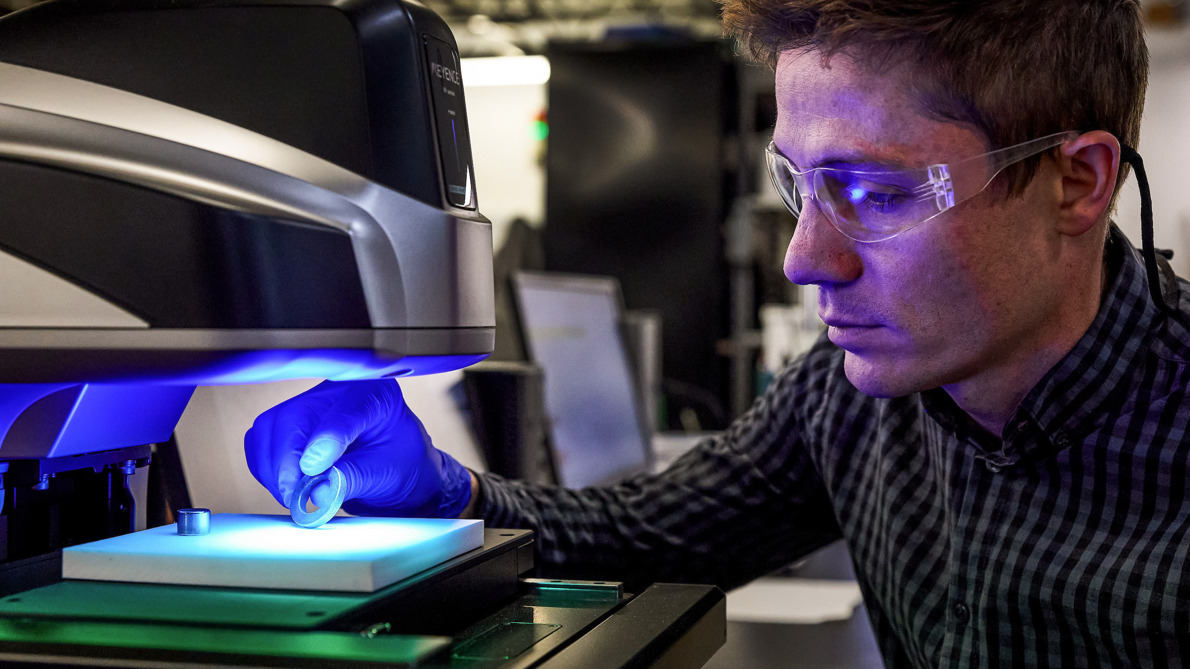 worker in safety goggles places a magnet on a testing stage