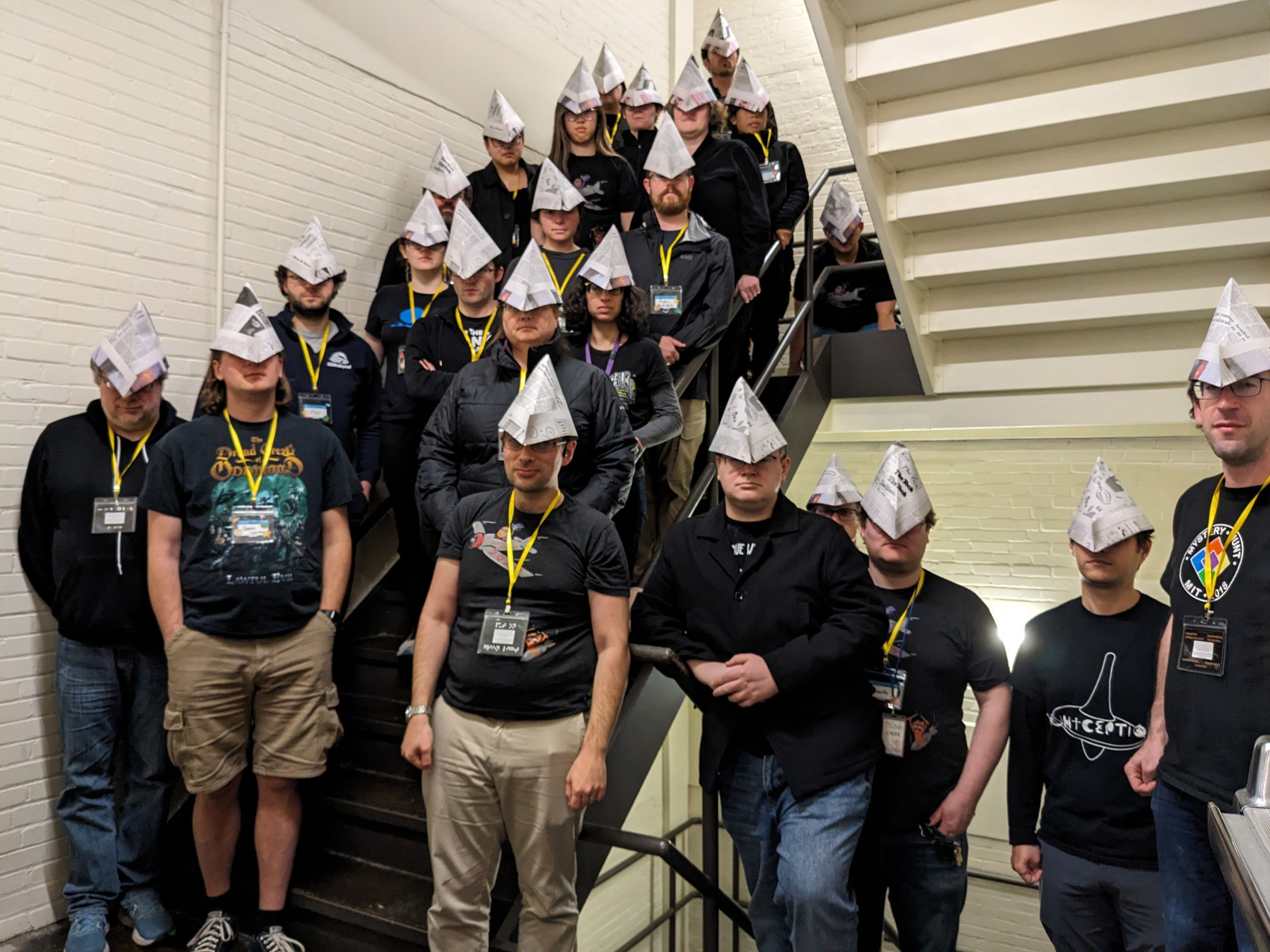 a group of people in a stairwell dressed in dark clothes with pointy paper hats.