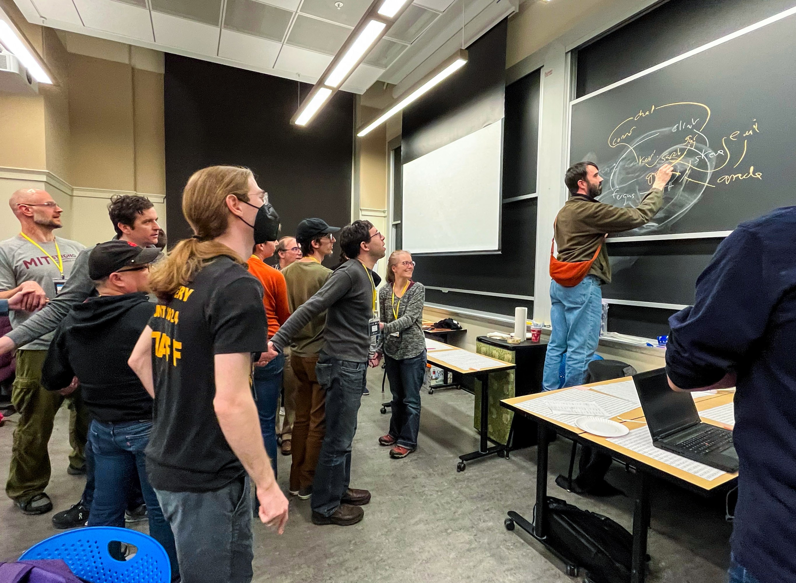 a group of people looking at a person writing at the chalkboard.