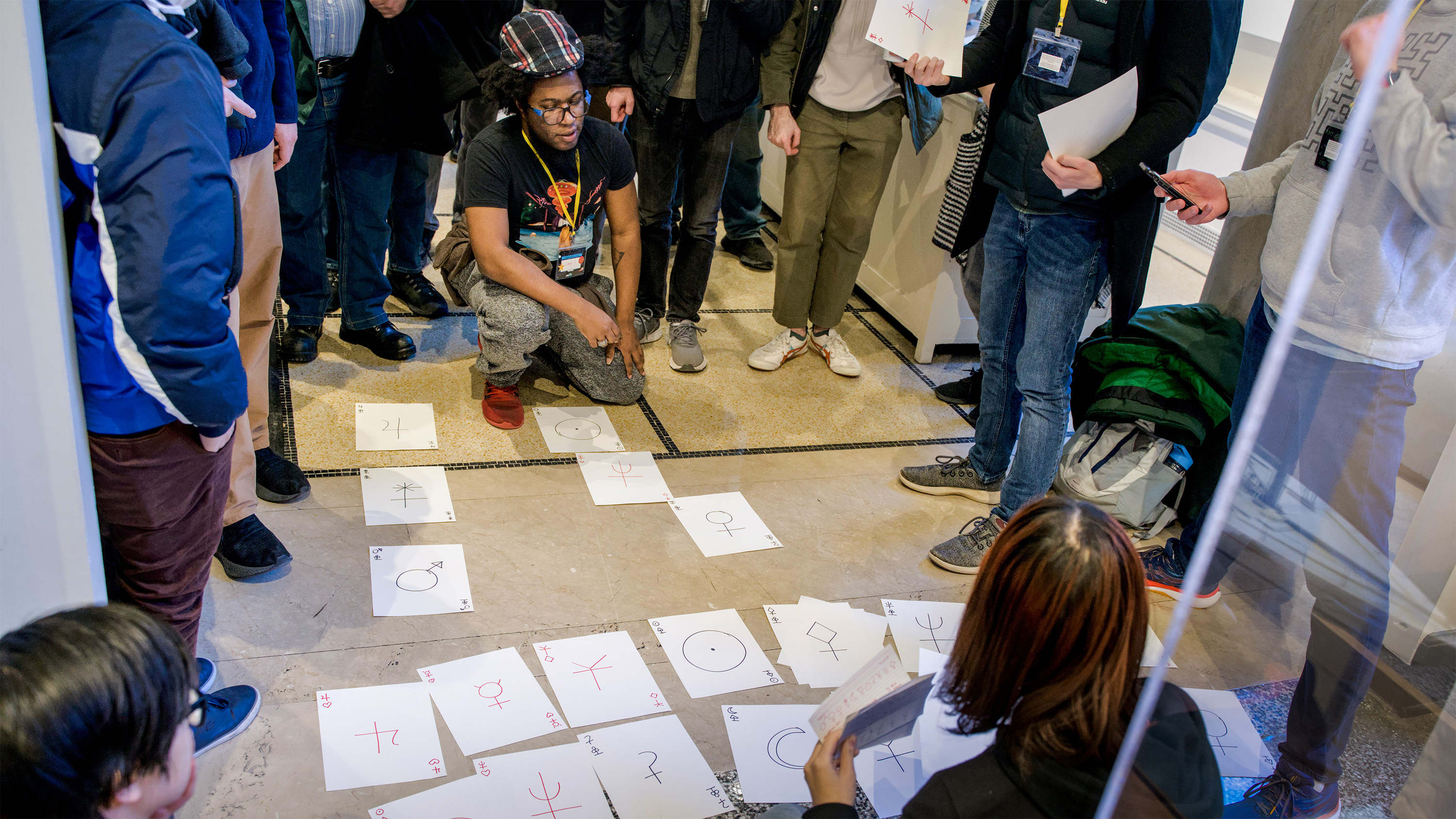 A group of people crouched to look at sheets of paper spread out on the floor.